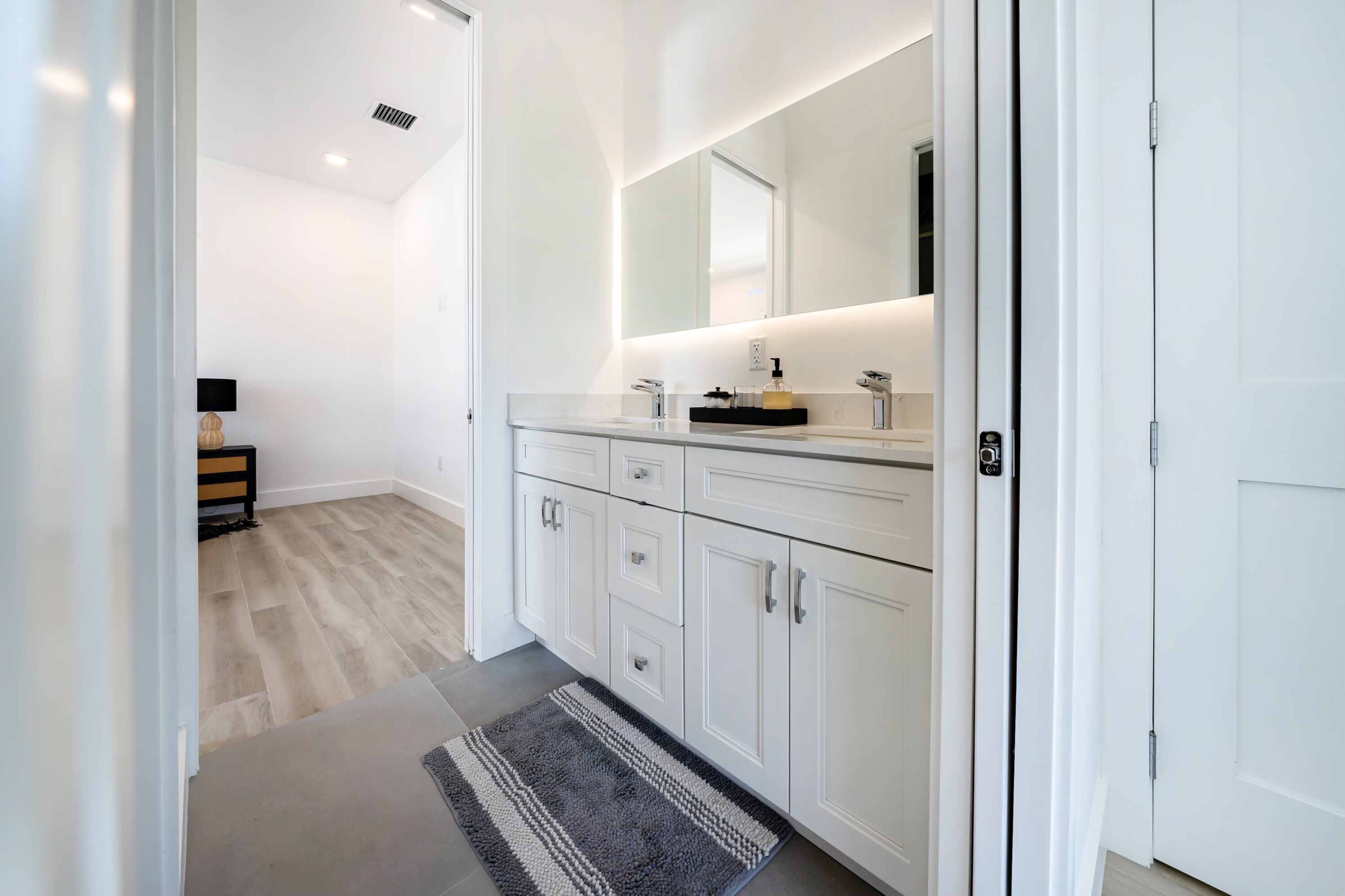 Een moderne badkamer met witte kastjes, een grote spiegel en een strak aanrecht.