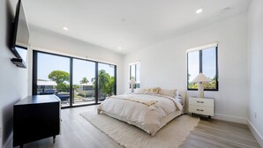 A modern bedroom with a large bed, a black dresser, and a nightstand. - ISLAMORADA DREAM (Islamorada)