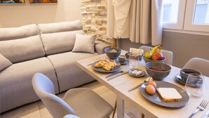 A modern living room with a sofa, dining table, and chairs. The room has a stone wall and a window with curtains. - Mariet Athens Spa (Athens)