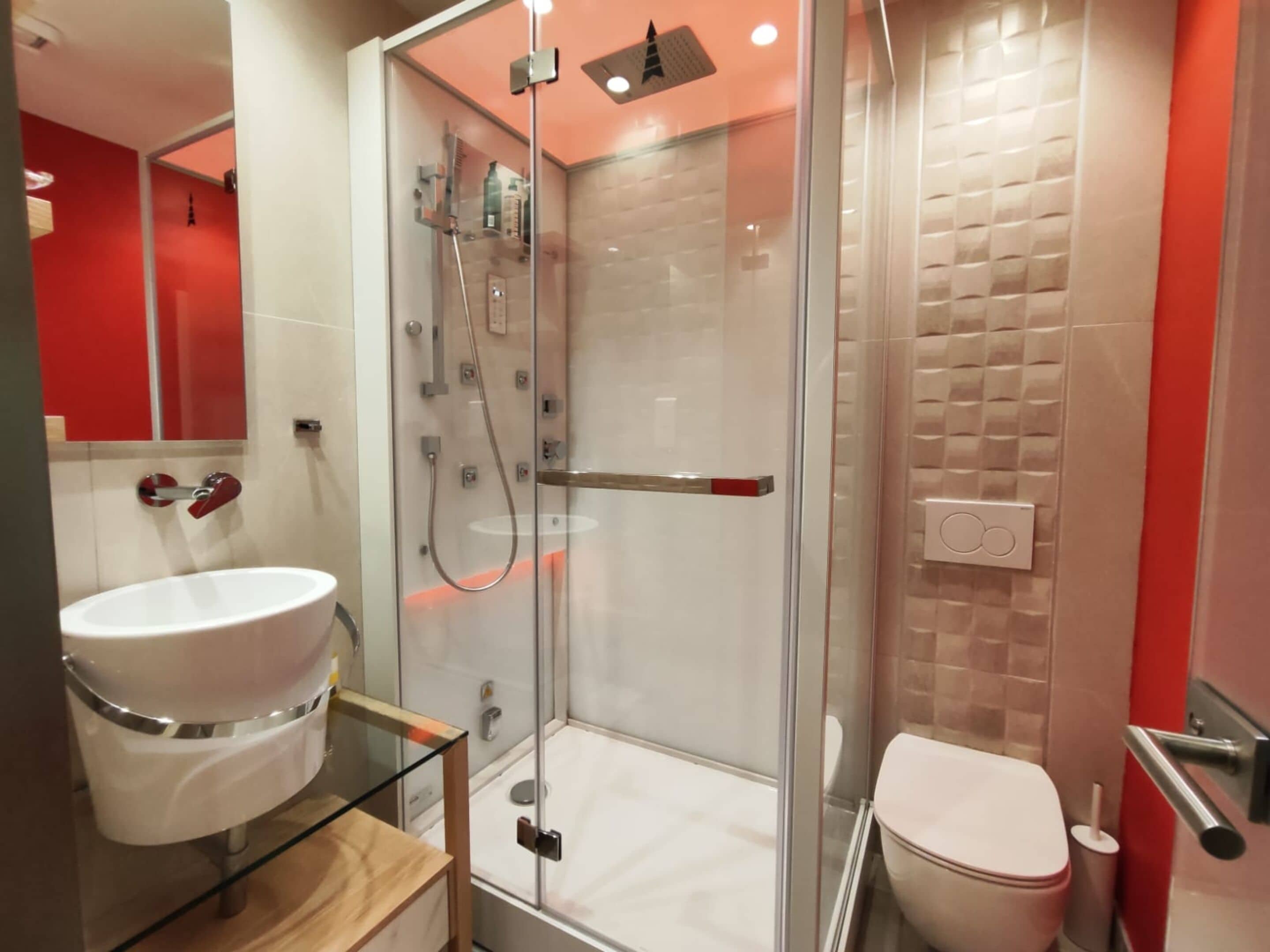 Een moderne badkamer met een douchekabinet van glas, een witte wastafel en een toilet.