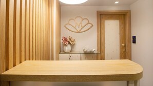 A reception desk with a wooden finish, a wall-mounted flower arrangement, and a door with a digital lock. - Mariet Athens Spa (Athens)