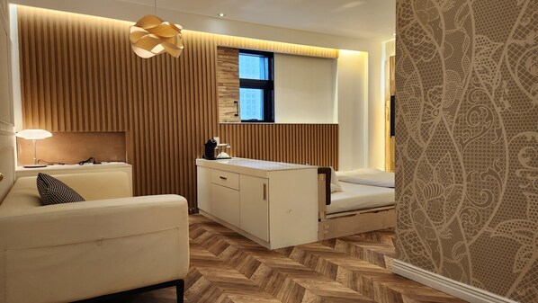 A compact hotel room with a sofa, a small desk, a bed, and a window.