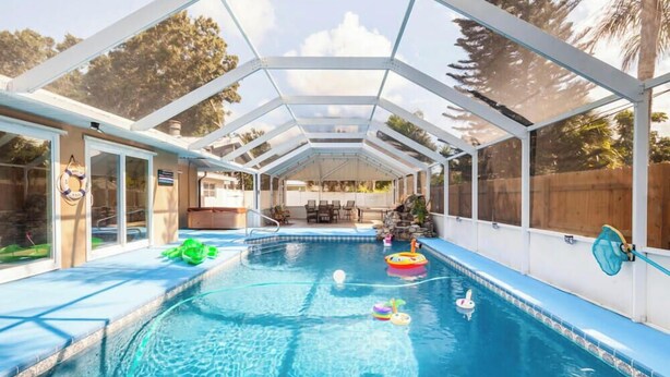 A covered swimming pool with clear glass panels, surrounded by a white metal frame. - Home with play room, enclosed pool . Only 10 minutes from the beach! (Vero Beach)