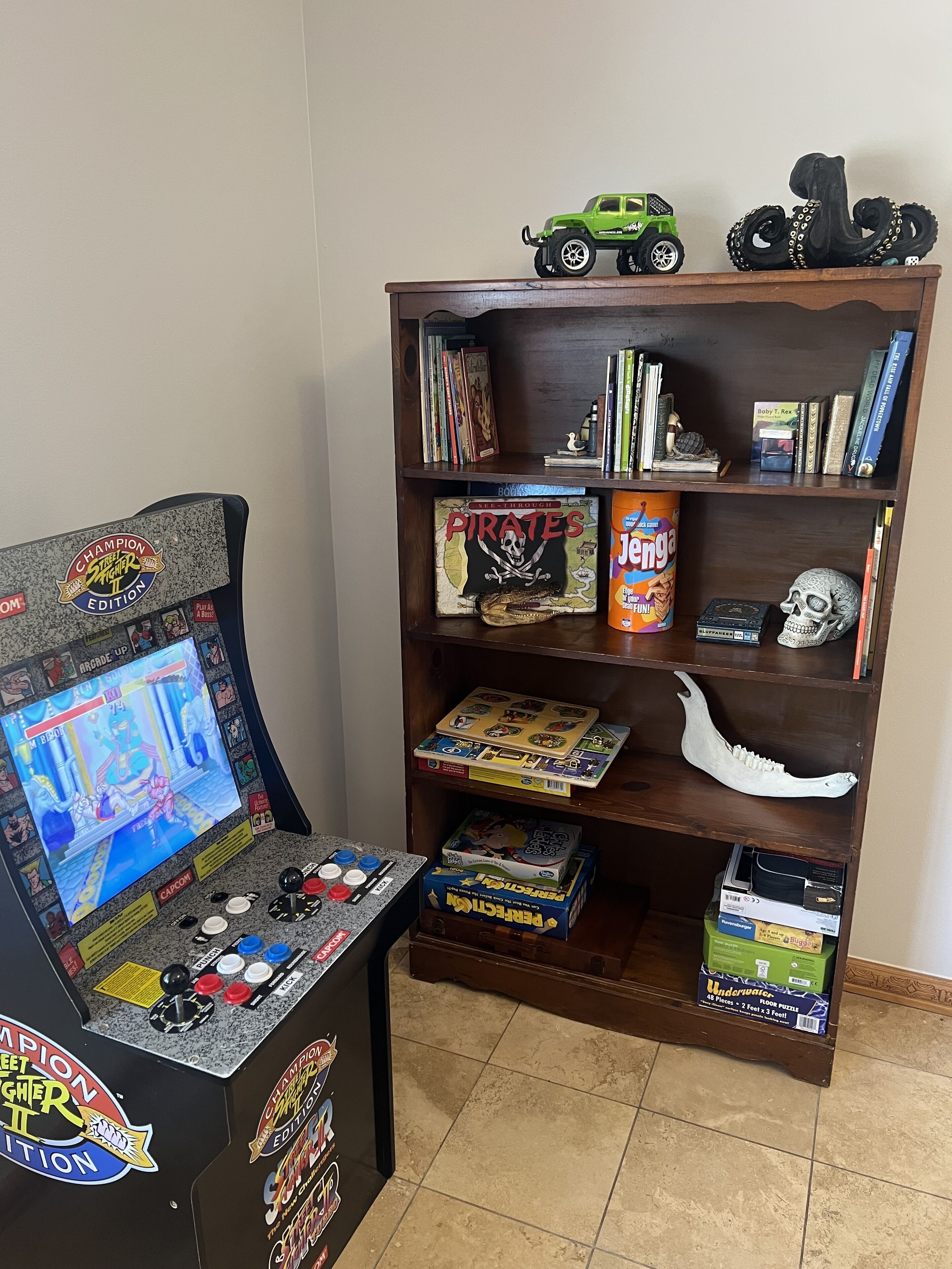 A room with a gaming console, a bookshelf, and various board games.
