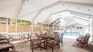 A covered patio area with a pool, wooden furniture, and a stone feature. - Home with play room, enclosed pool . Only 10 minutes from the beach! (Vero Beach)