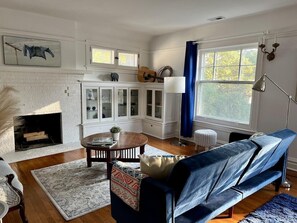 Una sala de estar con chimenea, un sofá azul, una mesa de centro redonda y un mueble con puertas de vidrio.