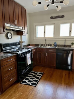 Una cocina con armarios de madera, estufa, horno, lavavajillas y una ventana sobre el fregadero.