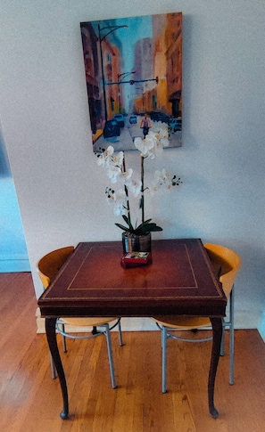 Una mesa de comedor con un jarrón de orquídeas blancas, un cuadro de un paisaje urbano y dos sillas.