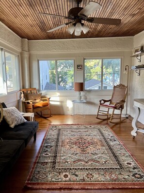 Una habitación con ventilador de techo, un tapete grande, un sillón mecedora, un sofá y una mesa.