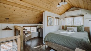 Une chambre confortable avec un plafond en bois, un grand lit, un fauteuil en osier et une petite table.