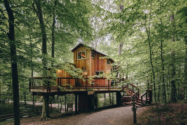Una cabaña de madera con un balcón y escaleras, rodeada por un bosque.
