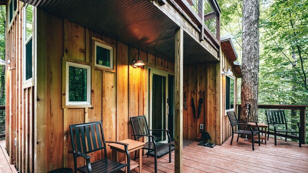 Une cabane en bois avec un porche, une terrasse en bois et deux chaises.