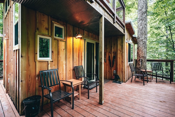 A wooden cabin with a porch, wooden deck, and two chairs.