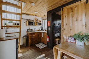 Eine Holz-Küche mit Kühlschrank, Spüle und Holzausziehtischen. Ein Feuerlöscher ist an der Wand befestigt und auf der Arbeitsplatte steht eine Pflanze.