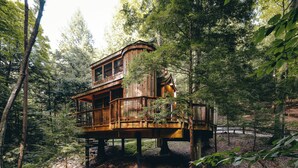 A wooden cabin with a balcony, surrounded by trees. - The Beech Treehouse | Hocking Hills (South Bloomingville)