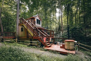 A wooden cabin with a staircase leading to a deck, surrounded by a forest. - The Beech Treehouse | Hocking Hills (South Bloomingville)