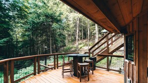 Une terrasse en bois avec une table et des chaises, entourée d’une zone boisée.