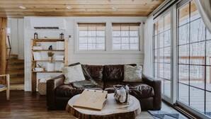 A cozy living room with a brown leather couch, wooden coffee table, and a bookshelf. - The Beech Treehouse | Hocking Hills (South Bloomingville)