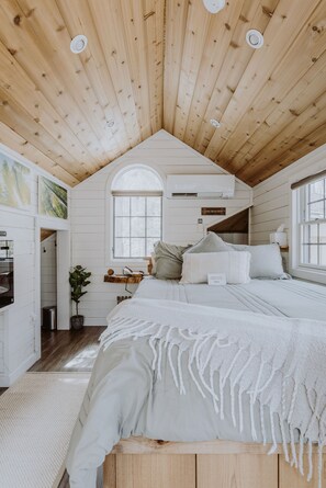 A cozy bedroom with a sloped ceiling, a large bed, a window, and a small desk area.