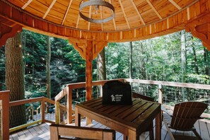 A wooden deck with a table and chairs, surrounded by a wooden railing, overlooking a forested area.