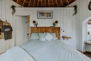 Un dormitorio con cabecera de madera, cama con colcha estampada, un cuadro enmarcado en la pared y una repisa con adornos.