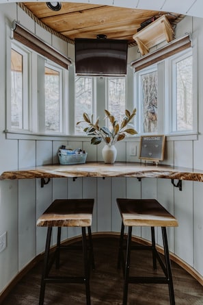 Eine rustikale Küche mit einer Holzausziehtafel, zwei Barhocker, einem Blumentopf und einem Willkommensschild.