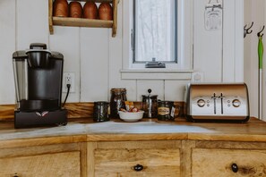 A kitchen with a coffee maker, a toaster, a jar of jam, and a window with a view of trees.