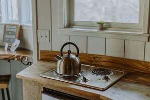 Une cuisine avec une bouilloire sur la cuisinière, une fenêtre avec une plante et un panneau accroché au mur.
