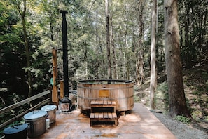 Eine Holzterrasse mit Whirlpool, umgeben von hohen Bäumen in einem Wald.