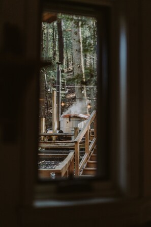 Un chalet rustique doté d’une terrasse en bois et d’une cheminée d’où s’échappe de la fumée, le tout entouré d’une forêt.