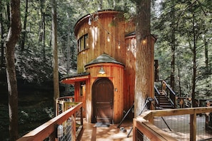 Ein hölzernes Baumhaus mit einer Holzterrasse, einer Treppe und einer Tür.