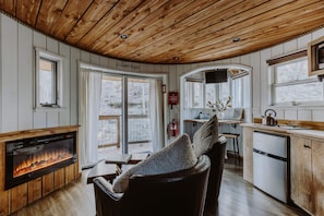 Interior acogedor de una cabaña con chimenea, techo de madera y una zona de cocina.