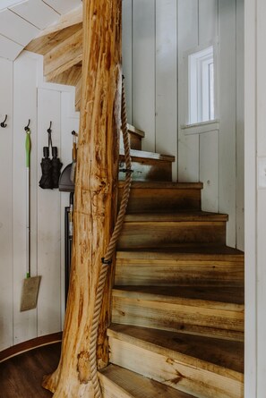 A wooden spiral staircase with a rope handrail, white walls, and a window at the top.