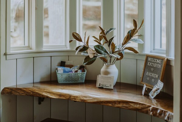 A reception area with a wooden counter, a vase with green leaves, a welcome sign, and a basket with items.