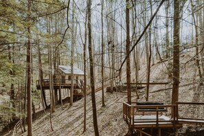 A forest cabin with a wooden deck and a small building.