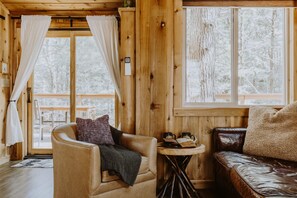 L’intérieur chaleureux d’un chalet, avec un décor en bois, un canapé en cuir, un fauteuil et une petite table sur laquelle se trouvent un livre et des tasses.