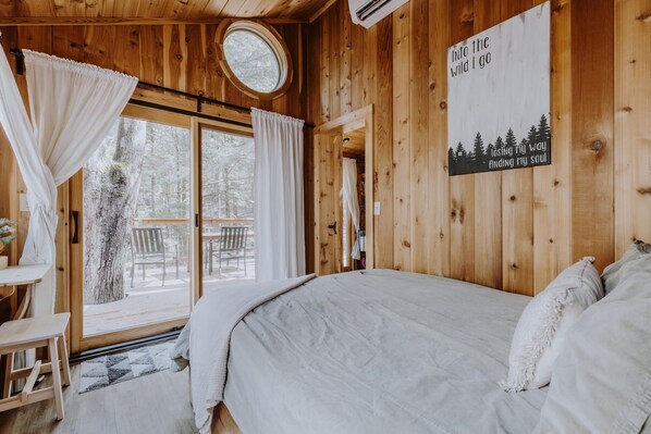 A wooden cabin bedroom with a bed, a window with curtains, a small table, and a sign on the wall.