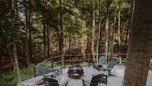 Een bebost gebied met een vuurkorf, omringd door Adirondack stoelen.