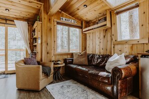A cozy cabin interior with a leather sofa, a small round table, and a bookshelf.