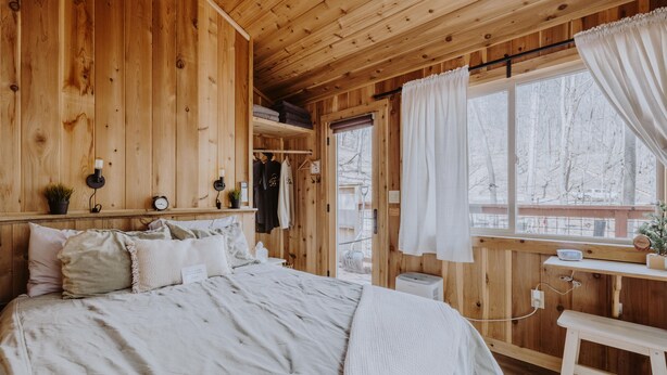 Een houten slaapkamer met een bed, nachtkastje en een raam met gordijnen.