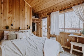A wooden cabin bedroom with a bed, bedside table, and a window with curtains.