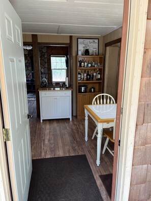 A compact kitchen with a stone wall, a built-in stove, and a wooden shelf with bottles.