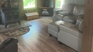 A cozy cabin interior with a stone fireplace, leather sofa, and a ceiling fan. - CABIN IN THE WOODS, 10 acres, Sleeps 8. Close to ORV trails and Forest Dunes. (Roscommon)