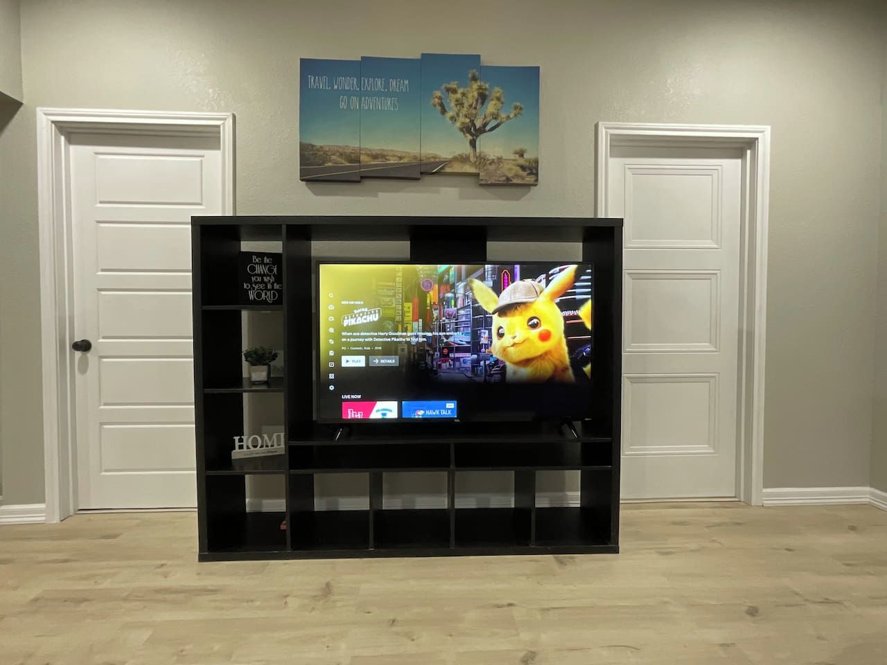 A flat-screen TV on a black stand in a room with a wooden floor and white walls.