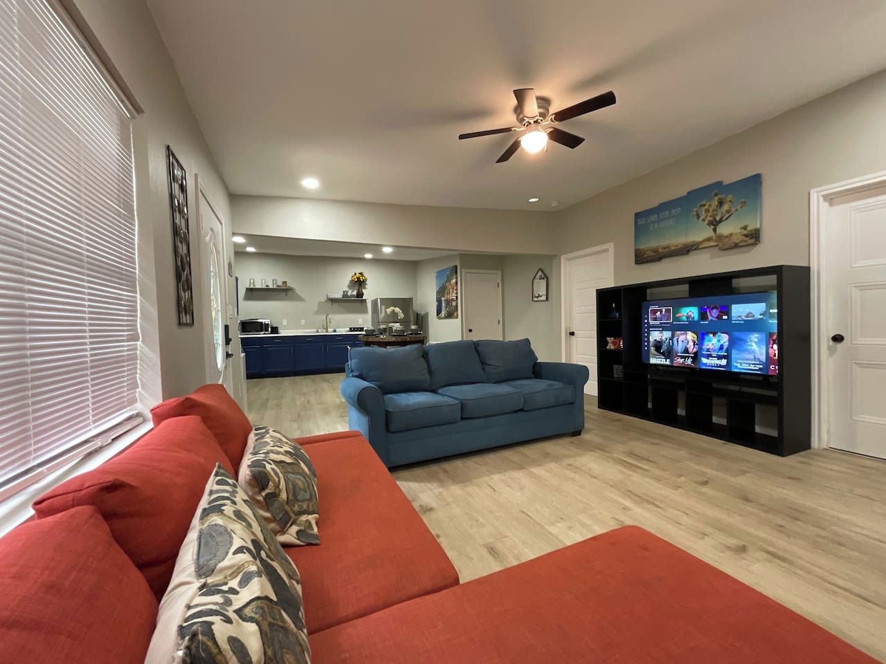 A living room with a red sofa, a blue sofa, a ceiling fan, and a TV on a black stand.