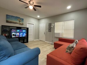 A living room with a flat-screen TV, two sofas, a ceiling fan, and a door.
