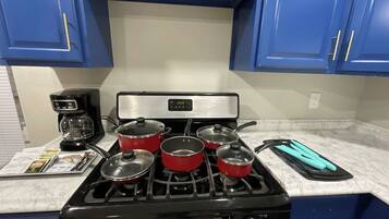 Una cocina con estufa a gas, cuatro ollas rojas, una cafetera y una encimera azul.