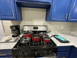 A kitchen with a gas stove, four red pots, a coffee maker, and a blue countertop.
