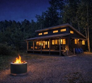 A cabin with a covered porch, a fire pit, and a view of the forest. - Deadwood Two Bit Cabin on the Creek (Sturgis)