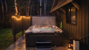 Un bain à remous avec des marches, un tuyau d’arrosage et une lanterne, situés à l’extérieur d’un bâtiment, de nuit.